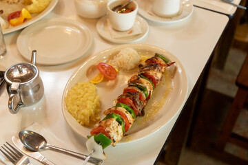 Delicious chicken and beef brochette served with rice, mashed potatoes, tomato and orange slices on a plate in a restaurant