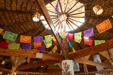 Traditional mexican papel picado banners decorating a palapa with a thatched roof, creating a...