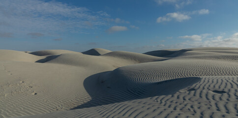 Sand dunes undulating beneath wispy clouds, revealing natural wind-carved textures and sweeping desert terrain