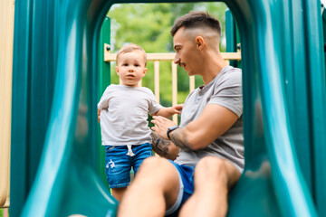 father with child boy is sitting on the slide with it