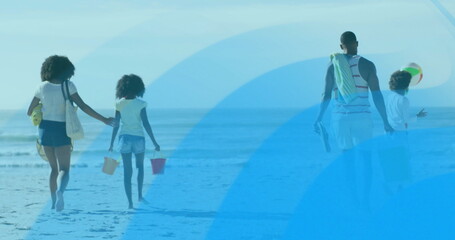 Walking family carrying sand buckets, colorful ball, beach towels toward calm ocean at sandy beach