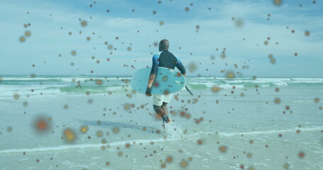 Stepping senior man in wetsuit entering shallow ocean water at sandy beach, with white surfboard