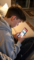 A teenager, engrossed in the world of viral videos, scrolls through the feed on his smartphone