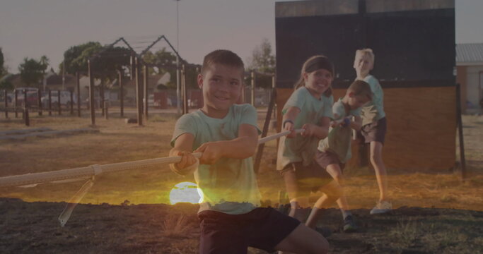 Pulling group of four boys tugging thick rope on playground grass, with wooden obstacle wall