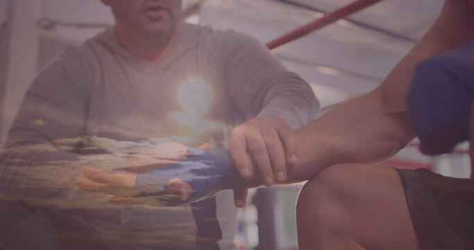 Trainer in grey shirt wrapping boxer's hands in boxing gym ring, with blue wraps, red ropes - Powered by Adobe