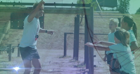 Instructor in sportswear pointing obstacle start to children on dirt with whistle, copy space