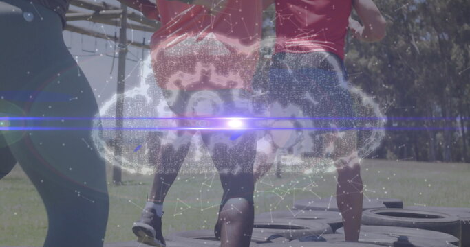 Four adults in athletic wear navigating rubber tire course in park, with digital cloud overlay - Powered by Adobe