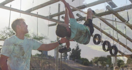 Steadying parent wearing sportswear supporting child hanging on monkey bars in park, hanging tires
