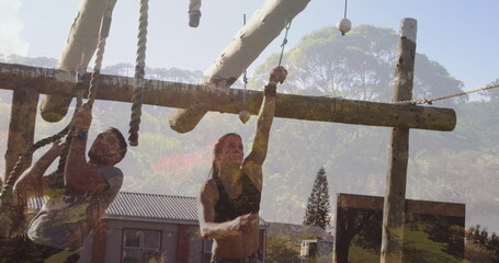 Climbing duo wearing sportswear navigating rope obstacles at outdoor course, with logs and beams