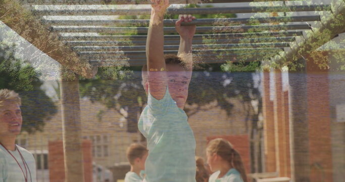 Boy hanging from monkey bars in playground, with coach wearing whistle and kids wearing matching t