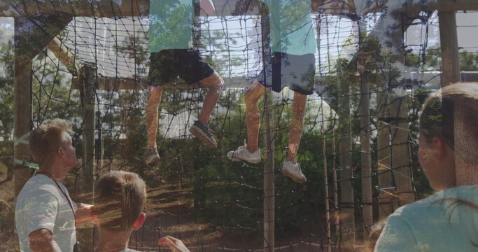 Climbing children dangling legs on rope netting in wooded park, with safety lanyard