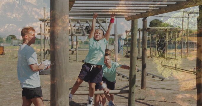 Gripping girl traversing metal monkey bars at outdoor course, with clipboard and balancing bar