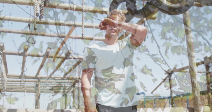Raising forearm, man wiping sweat at outdoor obstacle course, with beams ropes rings pulley wheel