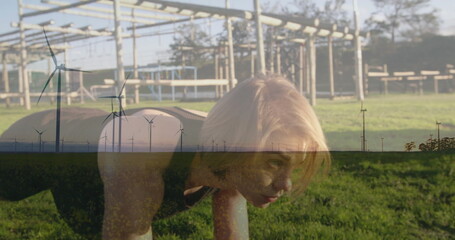 Holding low plank woman wearing athletic gear at grassy park, with climbing frame and wind turbines