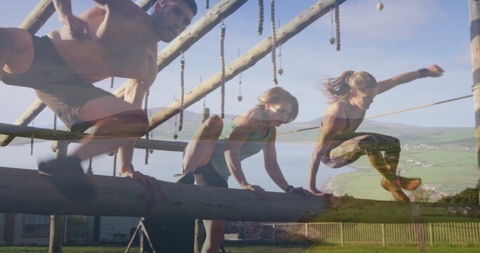 Climbing training partners navigating wooden obstacle course in grassy fenced field, ropes, beams
