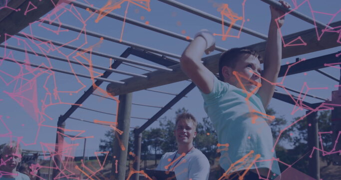Swinging boy in teal t-shirt crossing monkey bars at grassy obstacle course, wristbands, copy space