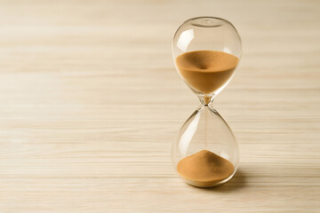 Glass hourglass with running sand on light wooden background, symbol of passing time, deadline pressure, countdown or patience concept, vintage timer for productivity, life, business, or time manageme
