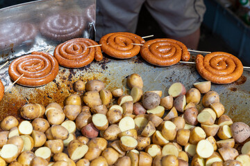 Cook grilling spiral sausages and potatoes on large hot plate