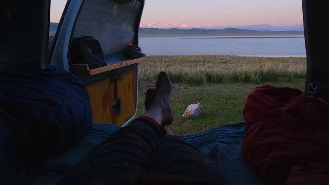 The door of a small camper opens, and there, a breathtaking view of the mountain lake Tuzkol and the snow-capped peaks of Khan-Tengri. Wild camping in Kazakhstan in the summer, peaceful moments 