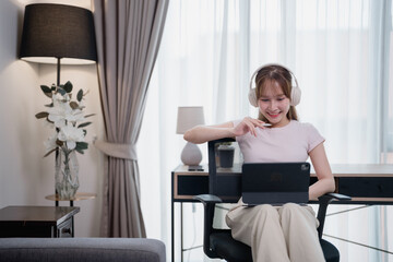 Young asian woman working from home using tablet and headphones, sitting on a comfortable chair in...