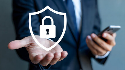 Confident businessman holding shield with padlock symbol, protecting digital data and mobile security, ensuring business safety.