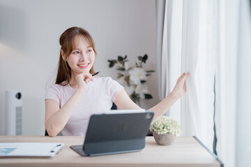 Young Asian businesswoman opening curtains and contemplating fresh ideas while working from home,...