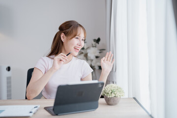 Young Asian businesswoman using a digital tablet, engaging in a video conference, smiling and...