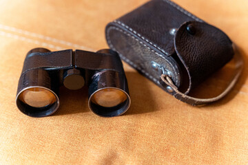 Vintage binoculars with leather case resting on sofa