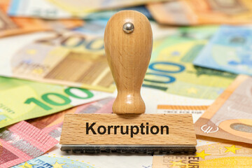 Ein Holzstempel ist beschriftet mit dem Aufdruck Korruption und steht über vielen Euro Banknoten