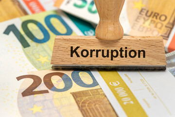 Ein Holzstempel ist beschriftet mit dem Aufdruck Korruption und steht über vielen Euro Banknoten