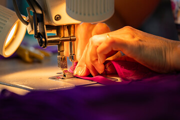 Zoom sur une machine à coudre en fonctionnement avec des mains en pleine action guidant le tissu, illustrant le geste précis de la confection artisanale.