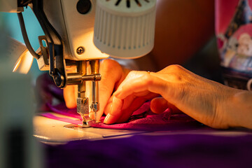 Zoom sur une machine à coudre en fonctionnement avec des mains en pleine action guidant le tissu, illustrant le geste précis de la confection artisanale.
