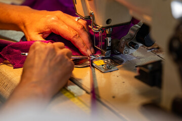 Zoom sur une machine à coudre en fonctionnement avec des mains en pleine action guidant le tissu, illustrant le geste précis de la confection artisanale.