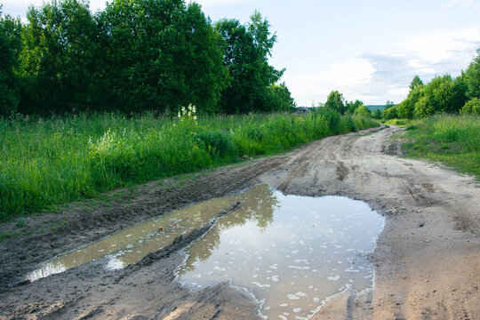 Large puddle blocking dirt road in green rural landscape