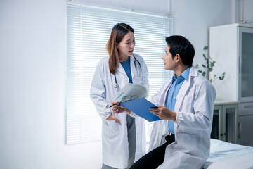 Two doctors are sitting in a hospital room, looking at a medical chart