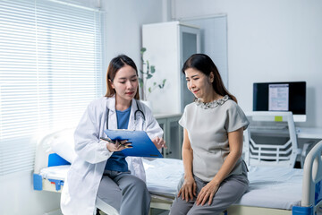 A woman is sitting on a hospital bed while a doctor looks at her