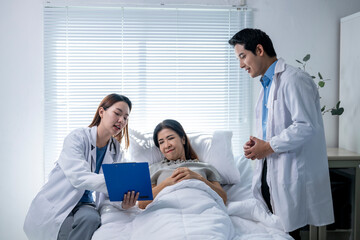 A woman is laying in bed with a doctor and a nurse looking at her