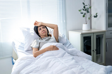 A woman is laying in bed with her hand on her forehead