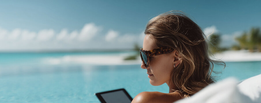 Woman relaxing poolside with tablet, turquoise sea backdrop. Illustrates luxury, escape, digital nomad lifestyle. Ideal for travel, tech, wellness themes.