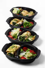 Omelette rolls with shrimp and red fish with herbs, served with salad mix and cherry tomatoes in black containers on a white background