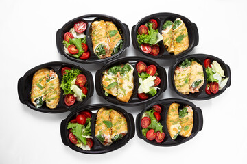 Omelette rolls with shrimp and red fish with herbs, served with salad mix and cherry tomatoes in black containers on a white background
