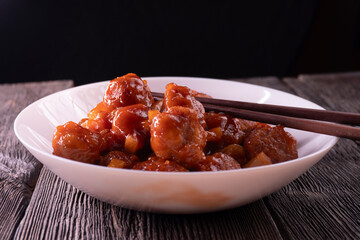Meatballs with pineapple in sweet and sour sauce on wooden background. Chinese food. Asian cuisine