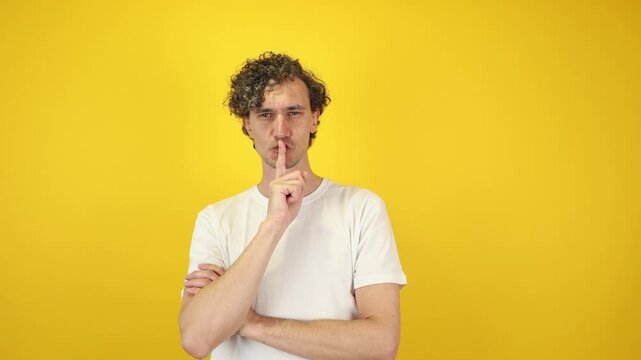 Playful young man, guy glances sideways, look aside, pressing finger to mouth lips in shhh sign. isolated yellow background studio. PR releases, soundless-themed spots, secrecy inspired banners.