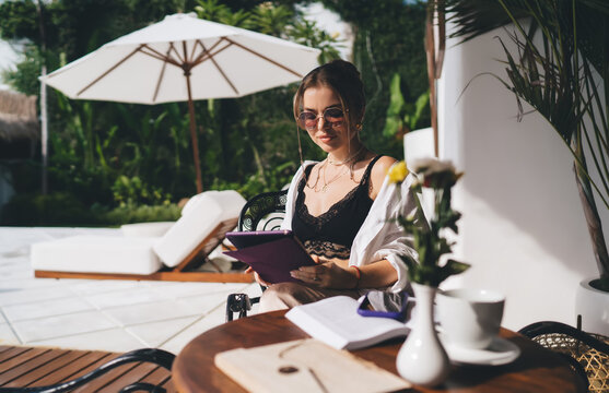 Focused freelancer woman using tablet by poolside, immersed in tech-based work. Scene captures concentrated workflow, modern freelancing and seamless digital lifestyle rhythm. - Powered by Adobe
