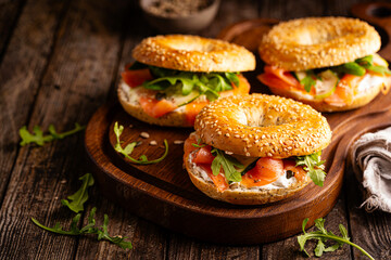 Healthy breakfast food. Bagel sandwich with salmon, cream cheese, cucumber and microgreens on wooden background. Burger with salmon.