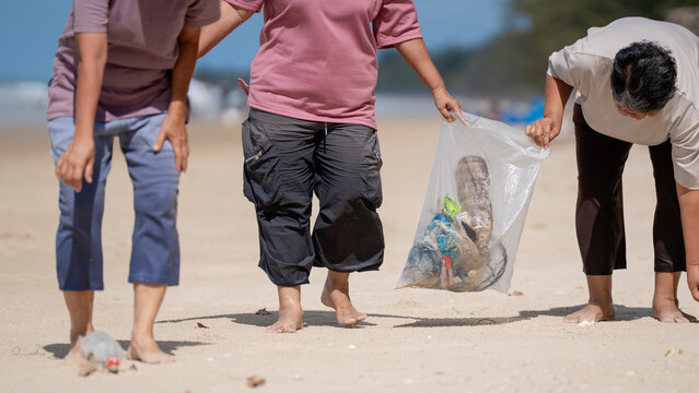 A group of older people are picking up trash on the beach to help keep nature clean and beautiful. - Powered by Adobe