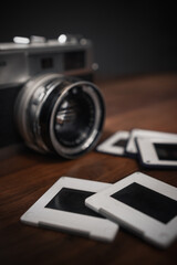 Vintage analog camera with lens and empty slides laying on wooden table against dark background representing memories, nostalgia, and traditional photography