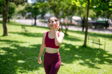 Fototapeta premium A woman wearing headphones and a red tank top is walking in a park