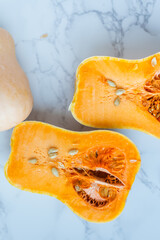 Halved butternut squash with seeds on marble surface.