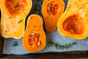 Seasoned butternut squash halves on baking tray with herbs.